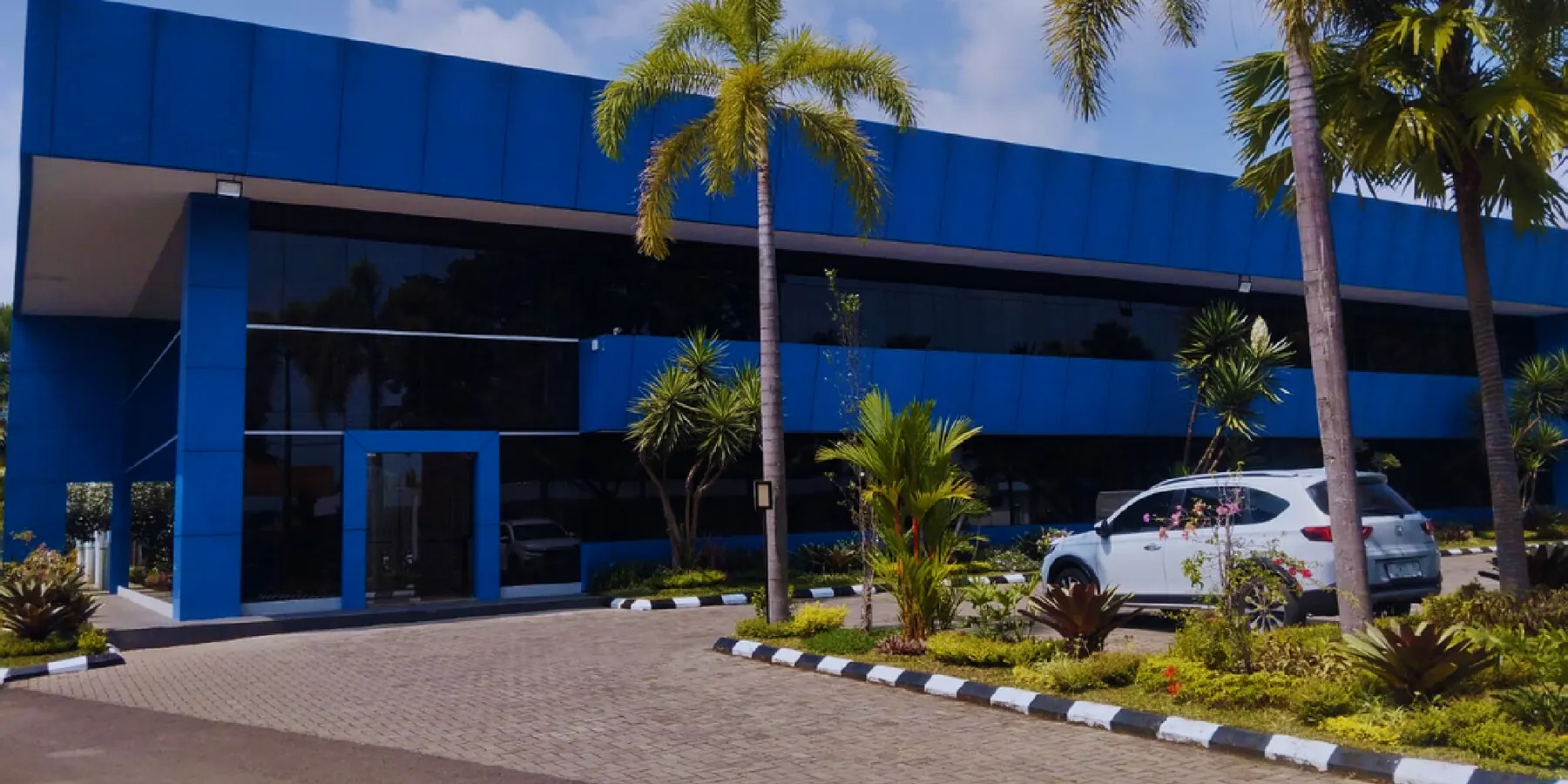 The blue PT Daux Cosmetic factory building among palm trees in Garut, West Java